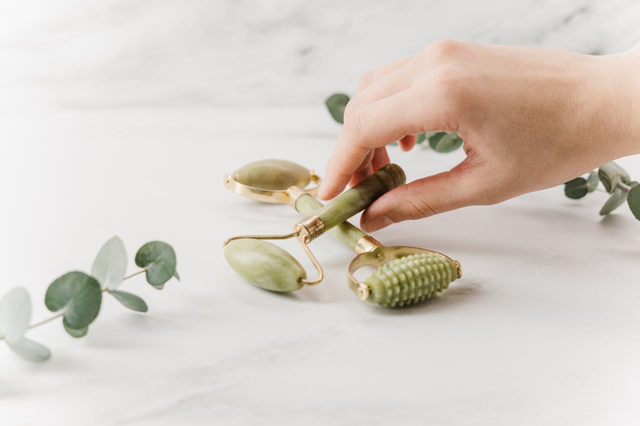 services-01 Close-up of a hand holding jade rollers on a marble surface for skincare and wellness.
