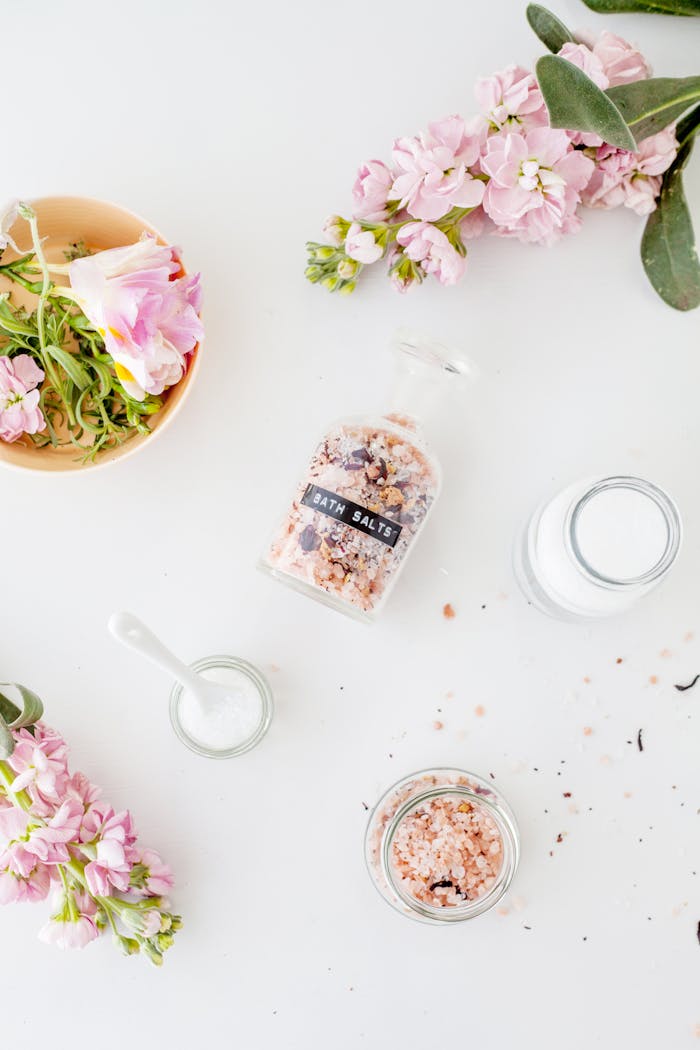 services-03 Top view of fresh delicate Brompton stock flowers with pink petals placed on white table with various jars of bath salts